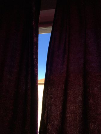 Blå himmel skymtar mellan fördragna gardiner